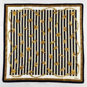 May include: A square silk scarf with a black and white striped pattern. The scarf features gold-colored decorative elements and a gold chain border. The text "ROMA ITALY FENDI" is printed around the border.