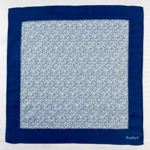 Peut inclure: Un mouchoir carré à motifs bleus et blancs. Le centre présente un fond blanc avec un délicat motif floral bleu. Une bordure bleu foncé uni encadre le motif floral. Le coin inférieur droit porte la mention "Margaret Howell".