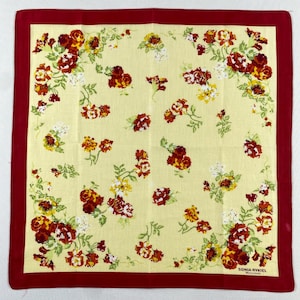 Peut inclure: Foulard carré jaune avec une bordure rouge et un motif floral. Le motif présente des roses rouges, jaunes et blanches avec des feuilles vertes. Le texte "SONIA RYKIEL" est imprimé en bas à droite.