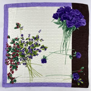 Peut inclure: Foulard carré en soie avec un fond blanc et une bordure violette. Le foulard présente des arrangements floraux de roses violettes et de baies rouges et bleues. Une bande verticale marron est sur le côté droit.