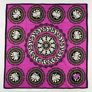 May include: A square, magenta-coloured handkerchief with a black border. The design features repeating circular patterns with white roses on a black background, and a central floral design. The text "ANNA SUI" is visible in the lower right corner.