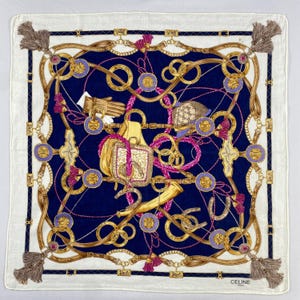 Peut inclure: Carré en soie blanc et bleu marine avec un motif équestre détaillé. L'écharpe présente des chaînes dorées, des accents violets et un centre bleu marine. Des glands sont aux coins, et la marque "CELINE" est visible.
