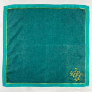 May include: Teal square handkerchief with a yellow border and corner accents. The handkerchief has a floral design in the bottom right corner. The border is a lighter shade of teal. The handkerchief is made of a soft material.