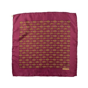 May include: A square, burgundy silk scarf with a repeating gold chain link pattern. The scarf has a subtle sheen and a small tag in the upper left corner. The lower right corner has the text "HERMES-PARIS".