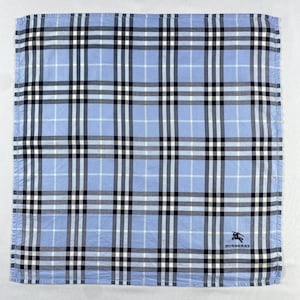 May include: A light blue square handkerchief featuring a plaid design in white, black, and navy blue. The Burberry logo is in the bottom right corner. The fabric is neatly folded. Measures approximately 30 cm x 30 cm.