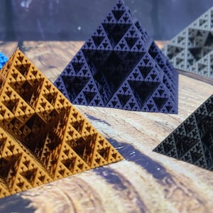 May include: Five 3D printed geometric pyramids in different colors: blue, gold, gray, black, and red. The pyramids are made of a textured material and have a fractal design.
