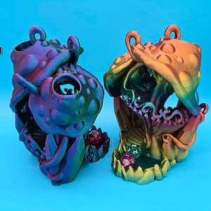 May include: Two 3D printed dice towers, one in a purple and green iridescent finish labelled "Magic Hummingbird" and the other in a rainbow iridescent finish labelled "Silk Rainbow".