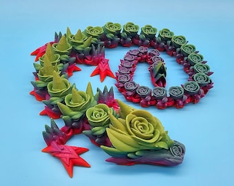 May include: A green, red, and purple dragon sculpture made of polymer clay. The dragon is covered in small, detailed rose-shaped flowers. The dragon is curled up in a coil shape.