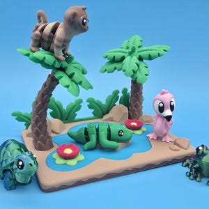 May include: A whimsical diorama featuring a miniature jungle scene with a monkey, palm trees, a crocodile, a flamingo, a turtle, and a frog. The scene is set on a brown base with a blue pond and red and yellow flowers, all against a blue backdrop.