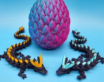 May include: Three 3D printed dragon figurines, one black with yellow accents, one black with blue accents, and one large dragon egg with blue and pink scales.