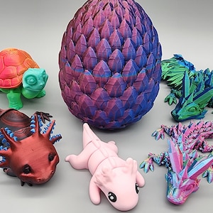 May include: A collection of 3D printed figurines, including a dragon egg, a turtle, an axolotl, and two dragons. The figurines are all brightly colored and have a textured, iridescent finish.