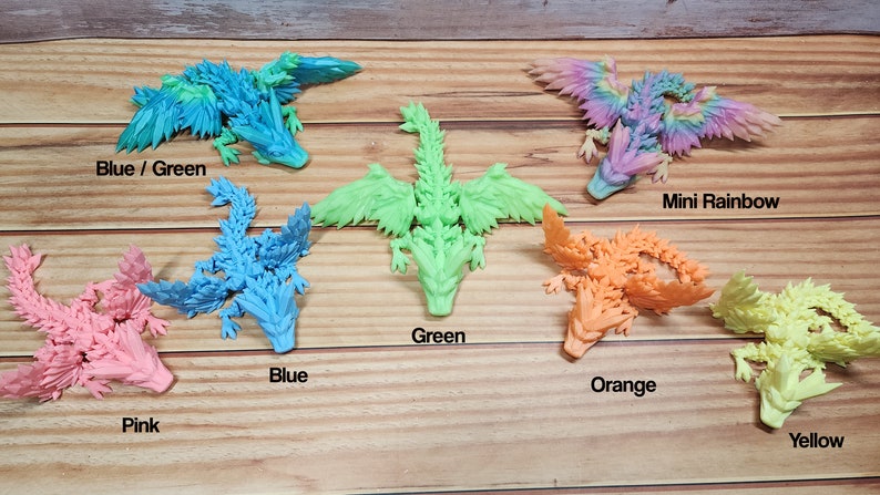 May include: A set of 7 colorful dragon figurines, each with a different color: blue/green, blue, green, orange, pink, yellow, and rainbow. The dragons are made of a textured material and have wings and tails.