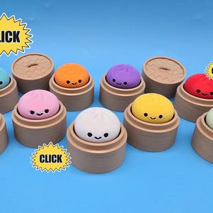 May include: A collection of small, colourful dumpling-shaped erasers, each resting in a miniature tan bamboo-style steamer basket. The erasers feature simple, smiling faces and come in blue, teal, pink, orange, purple, yellow, red, white, and light green.