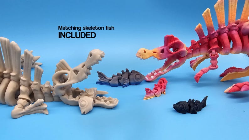 Pu&ograve; includere: Un set di giocattoli scheletrici articolati, tra cui un dinosauro rosa e arancione, un pesce grigio e un pesce nero. Il testo "Matching skeleton fish INCLUDED" &egrave; visibile nell'immagine.