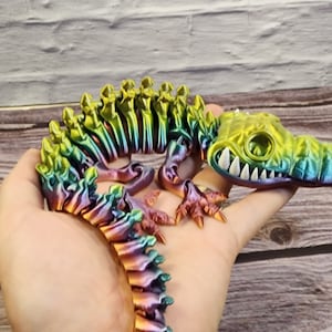 May include: A colourful, iridescent, skeletal crocodile figurine with a toothy grin. The figurine is made of a shiny, metallic material and has a rainbow-like colour scheme.