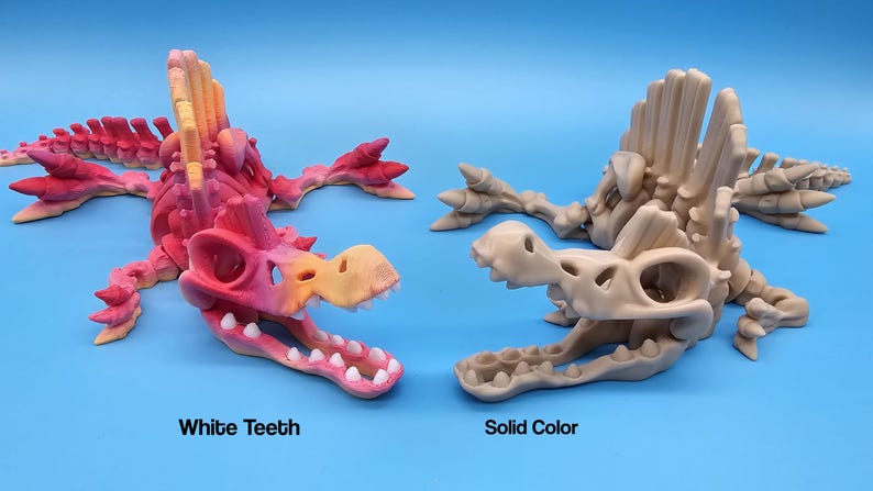 Pu&ograve; includere: Due scheletri di dinosauro stampati in 3D, uno con denti bianchi e un gradiente rosa e arancione, l'altro in beige solido.  "White Teeth" e "Solid Color" sono etichettati sotto ogni scheletro.