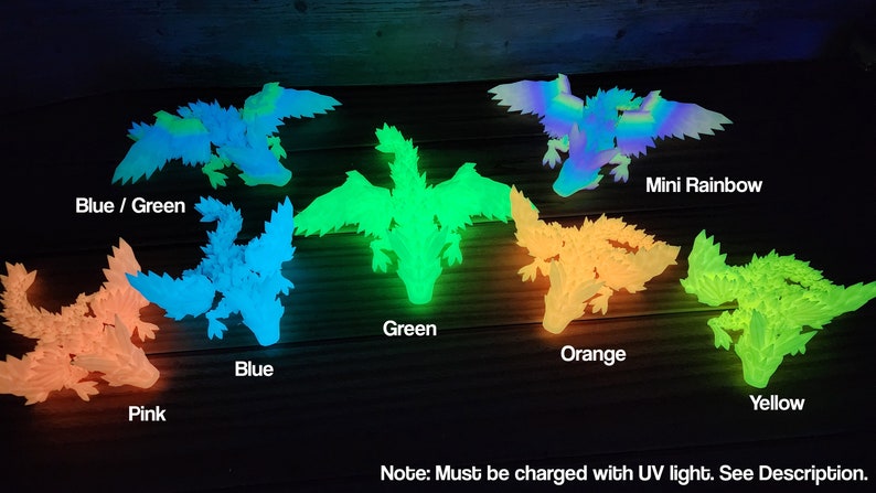 May include: A set of glow-in-the-dark dragon figurines in various colors, including pink, blue, green, orange, yellow, and a multi-colored rainbow dragon. The text "Note: Must be charged with UV light. See Description." is visible at the bottom of the image.