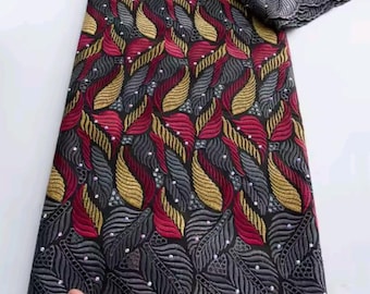 May include: A folded fabric with a detailed pattern. The fabric features a repeating design of stylized leaves in red, gold, and gray on a black background. The edges are finished with a decorative border. The text "Kalume" is visible at the top.