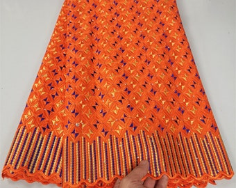 May include: Orange embroidered lace fabric with a geometric pattern and gold and blue accents. The fabric has a scalloped edge.