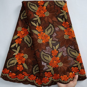 Puede incluir: Tela de encaje bordada en marrón y naranja con un patrón floral. La tela tiene un borde festoneado.