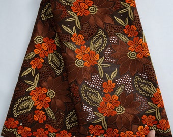 May include: Brown and orange embroidered lace fabric with a floral pattern. The fabric has a scalloped edge.