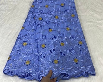 May include: A light blue fabric with an embroidered floral pattern. The design features large flowers with gold centers and small, sparkling accents. The fabric is folded, revealing the intricate details of the lace.