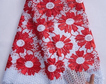 May include: Red and white floral lace fabric with a scalloped edge. The lace has a delicate, intricate design.