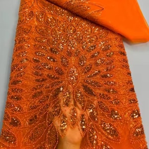 May include: Orange beaded fabric with a detailed floral pattern. The fabric is embellished with sequins and small beads, creating a textured, shimmering effect. The design is reminiscent of a peacock's feathers.