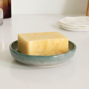 May include: A bar of yellow soap in a green ceramic soap dish.