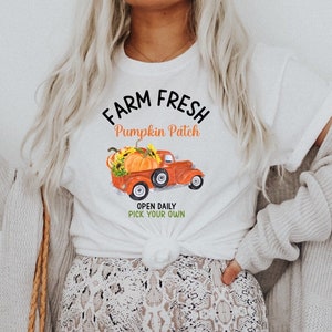 Op de afbeelding: Wit T-shirt met de tekst "Farm Fresh Pumpkin Patch" en een rode vrachtwagen met pompoenen in de laadbak. De tekst "Open Daily Pick Your Own" staat onder de vrachtwagen.