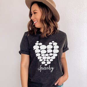 May include: Dark grey heather t-shirt with a white heart design made of speech bubbles. The text "Speechy" is written below the heart.