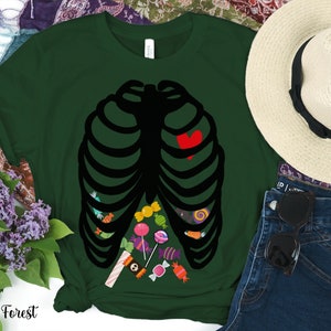 May include: A dark green t-shirt with a black skeleton ribcage design. The ribcage is filled with colorful candy and a red heart. The shirt is a fun and festive Halloween costume.