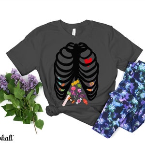 May include: A dark gray t-shirt with a black skeleton outline filled with colorful candy. The skeleton has a red heart in the center of its chest.