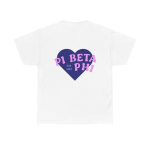 Könnte beinhalten: Weißes T-Shirt mit einem marineblauen herzförmigen Aufdruck. Das Herz enthält den Text "PI BETA PHI EST. 1867" in Hellviolett. Das T-Shirt besteht aus einem weichen, bequemen Material.