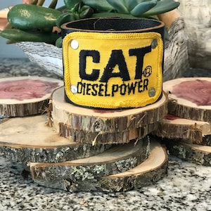 Può includere: Braccialetto in pelle nera con una toppa gialla che dice "CAT® DIESEL POWER".