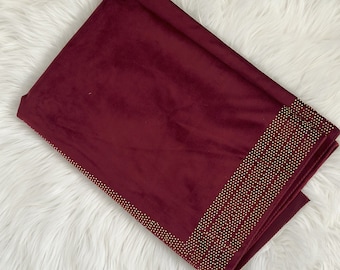 May include: A burgundy velvet scarf with a gold beaded trim. The scarf is folded and laid out on a white fluffy surface.