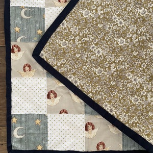 May include: A patchwork quilt with a floral pattern on the back. The front of the quilt is made up of different squares with various patterns, including stars, moons, polka dots, and angels.