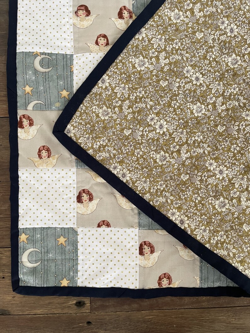May include: A patchwork quilt with a floral pattern on the back. The front of the quilt is made up of different squares with various patterns, including stars, moons, polka dots, and angels.