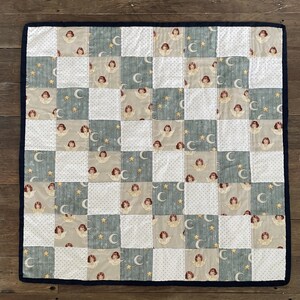 May include: A patchwork quilt with a blue, white, and beige pattern. The quilt features a repeating design of angels and crescent moons.
