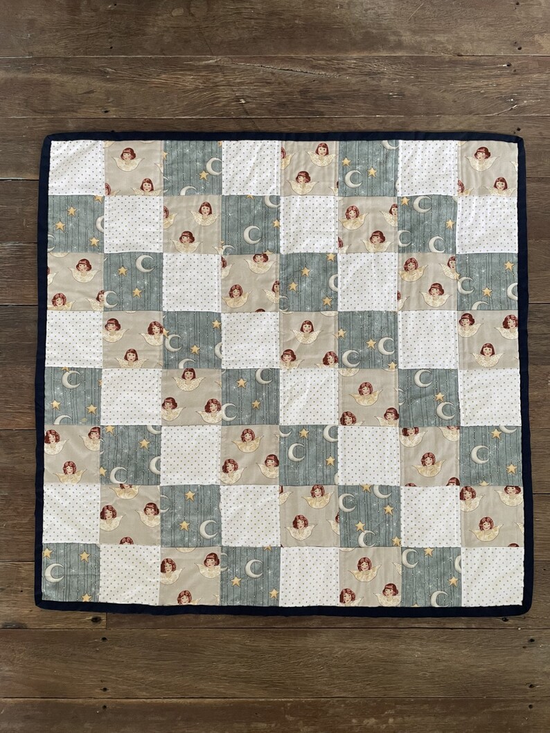 May include: A patchwork quilt with a blue, white, and beige pattern. The quilt features a repeating design of angels and crescent moons.