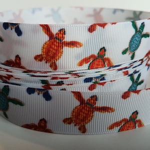 May include: White ribbon with a repeating pattern of colorful sea turtles. The turtles are in shades of orange, blue, and green. The ribbon is rolled up, showing the pattern on the edges.