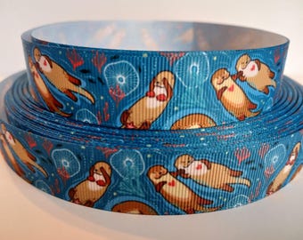 Op de afbeelding: Rol turquoise lint met een herhalend patroon van cartoonotters. De otters zijn bruin met rode harten, tegen een achtergrond van wit en rood zeeleven. Ideaal voor knutselen.