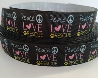 Peut inclure: Ruban noir imprimé avec les mots "Peace, Love, Rescue" en blanc, rose et jaune. Le motif comprend des symboles de paix, des cœurs et des empreintes de pattes. Le ruban est enroulé.