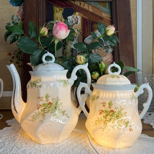 Könnte beinhalten: Ein Set aus zwei weißen Porzellan-Teetassen mit floralem Design. Die Tassen sind von innen beleuchtet und erzeugen ein warmes Leuchten. Die Tassen stehen auf einer weißen Spitze.