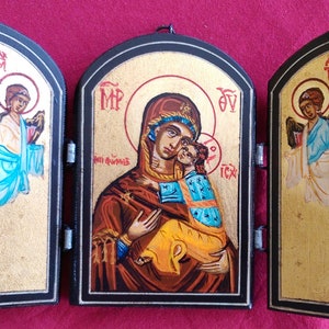 May include: A wooden triptych icon with a gold background. The center panel depicts the Virgin Mary holding the baby Jesus. The left and right panels depict angels with wings. The icon is painted in a traditional style.
