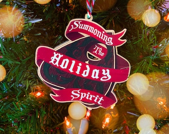 Puede incluir: Un adorno navideño rojo y dorado con el texto "Summoning the Holiday Spirit" en él.