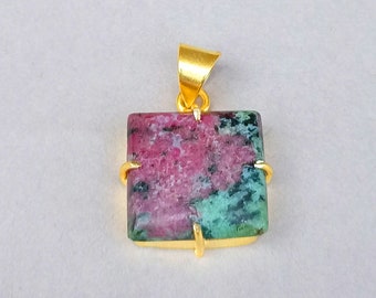 May include: A square pendant featuring a polished ruby zoisite stone with mottled pink and green coloration. The stone is set in a gold-toned metal frame with four prongs and includes a gold-toned triangular bail at the top for hanging.