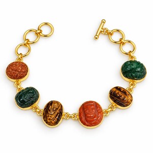Puede incluir: Una pulsera de tono dorado con seis dijes de escarabajo tallados en piedras preciosas de forma ovalada en varios colores, incluyendo naranja, verde y marrón. La pulsera está unida por eslabones circulares dorados y tiene un cierre de barra.