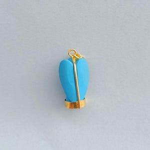 Op de afbeelding: Een turquoise blauwe hartvormige hanger met een gouden beugel en een gouden draad gewikkeld rond het hart. De hanger is op een witte achtergrond.