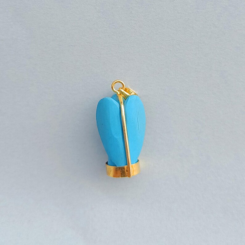 Op de afbeelding: Een turquoise blauwe hartvormige hanger met een gouden beugel en een gouden draad gewikkeld rond het hart. De hanger is op een witte achtergrond.